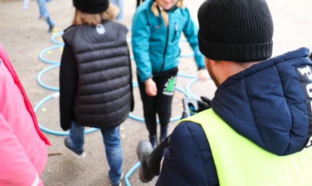 Lärare med reflexväst, framför honom några barn som kliver i ringar på skolgården. 
