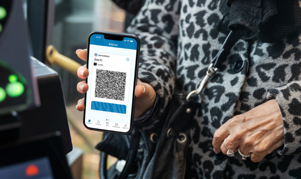 Bilden är beskuren så man ser en äldre persons händer där hen håller upp en mobil med en västtrafik-biljett.